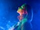 Young woman in neon blue light on smoke,steaming background. Lady in trench coat